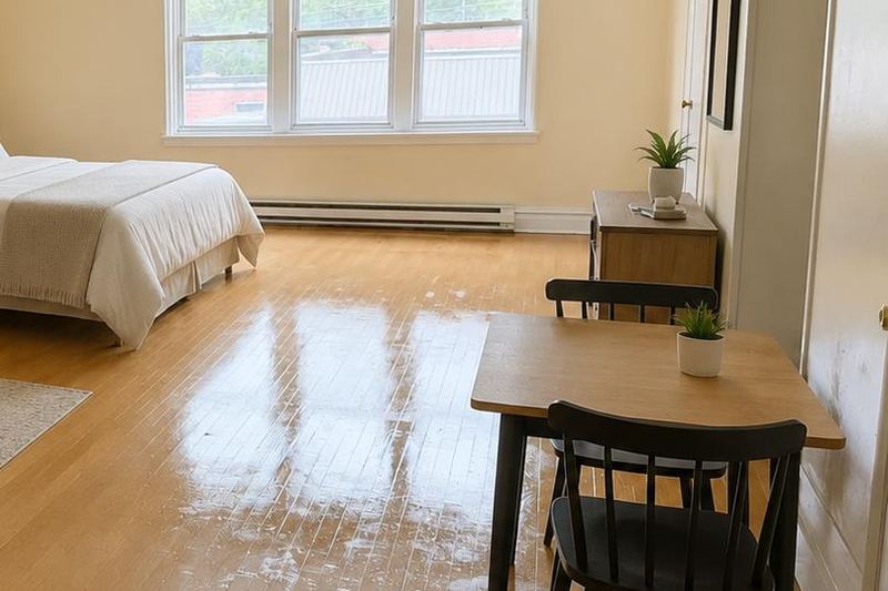 Queen bed and dining table beside large windows in a furnished Meadow River Lofts apartment